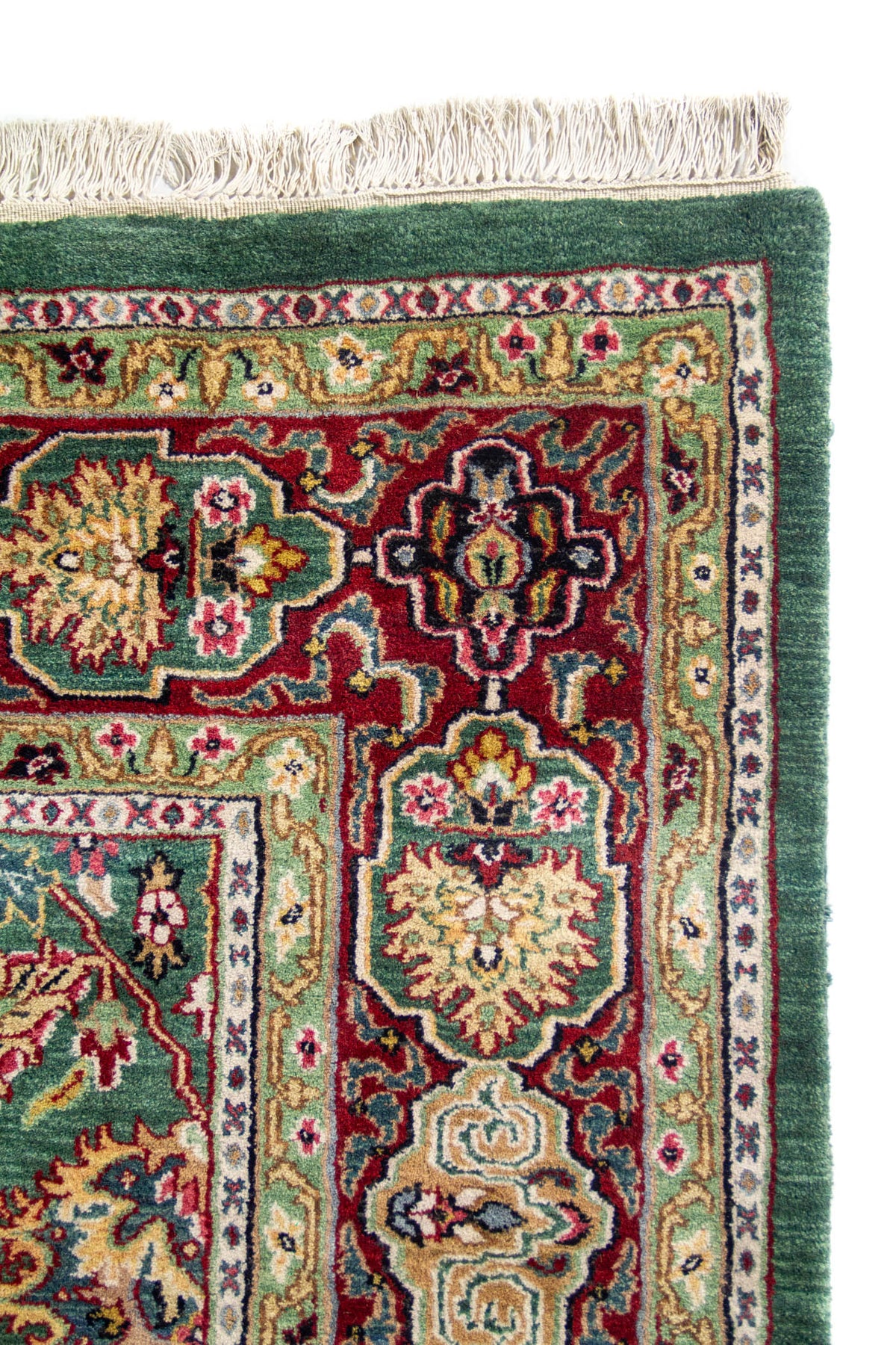 Detalle de esquina de alfombra oriental con flecos blancos, borde y guarda verde con motivos florales.