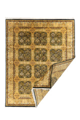 Alfombra oriental dorada con esquina doblada, mostrando el reverso y su diseño de paneles florales sobre fondo oscuro.