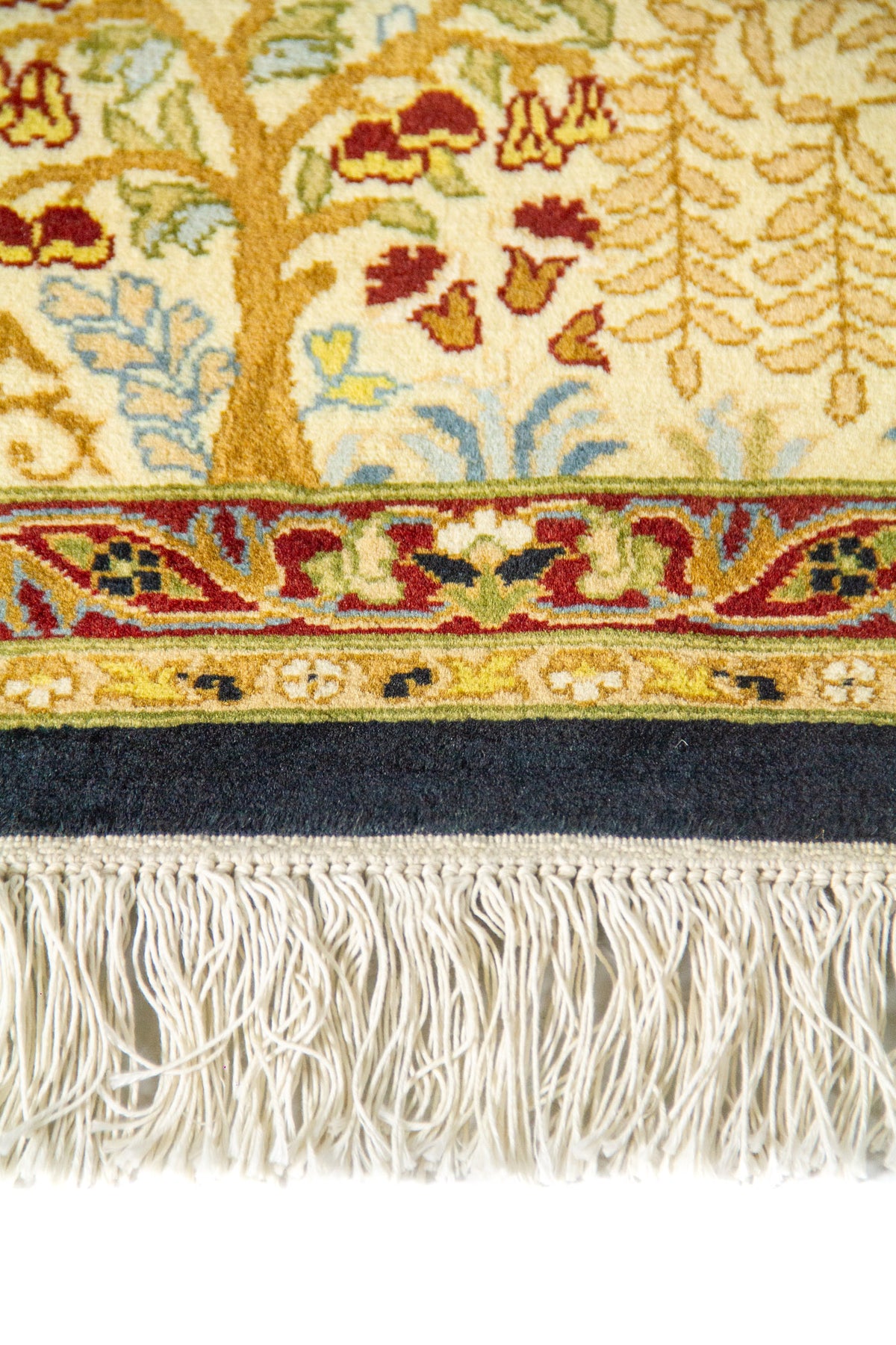 Detalle de flecos y borde de alfombra oriental con guarda beige y motivos botánicos en tonos dorado, rojo y azul.