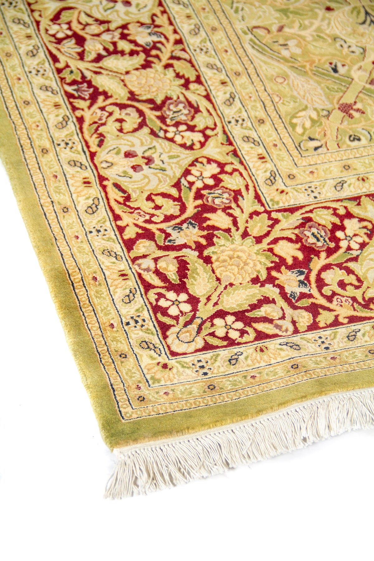 Detalle en ángulo de la esquina de alfombra clásica con guarda floral roja, franja beige y flecos blancos visibles.