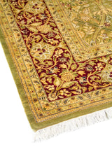 Primer plano de esquina de alfombra oriental en tonos verde, beige y rojo vino, con diseño floral ornamental y acabado con flecos.