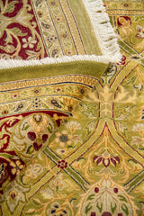 Detalle de alfombra doblada mostrando textura del tejido y motivos florales entrelazados en verde oliva, beige y rojo burdeos.