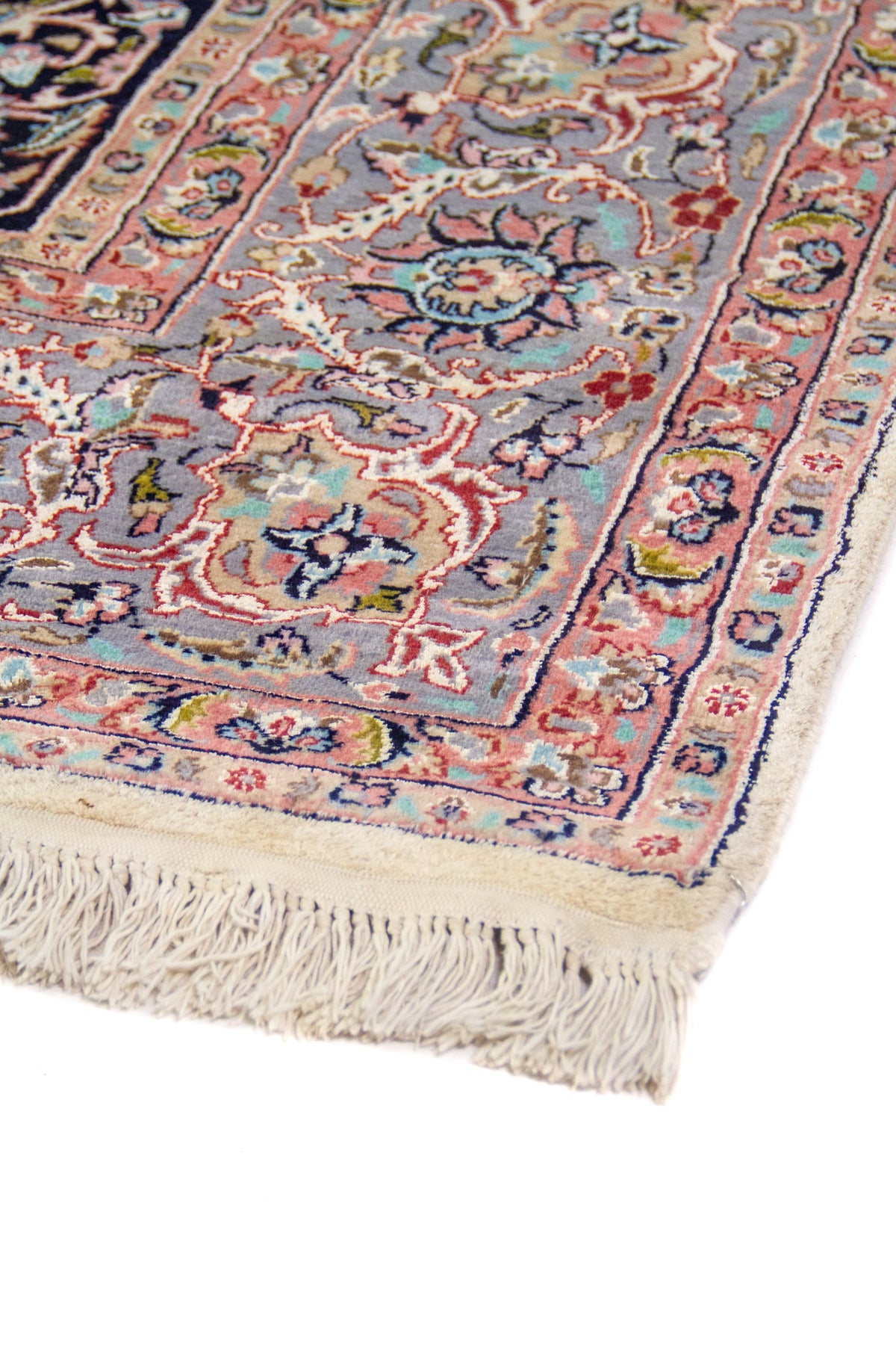 Detalle lateral en perspectiva de alfombra persa con patrones florales en azul y rosado.