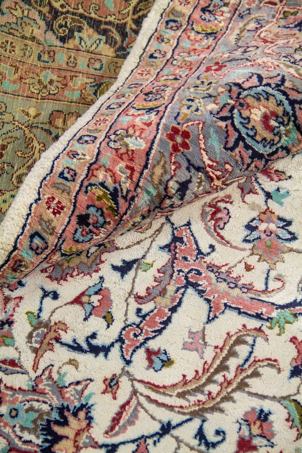 Detalle de pliegue de alfombra persa mostrando textura del tejido, diseño floral intrincado y combinación de colores pastel.