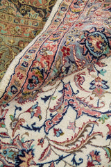 Detalle de pliegue de alfombra persa mostrando textura del tejido, diseño floral intrincado y combinación de colores pastel.