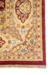 Detalle de esquina de alfombra clásica con guarda beige, fondo rojo vino y flecos, con motivos florales ornamentales.