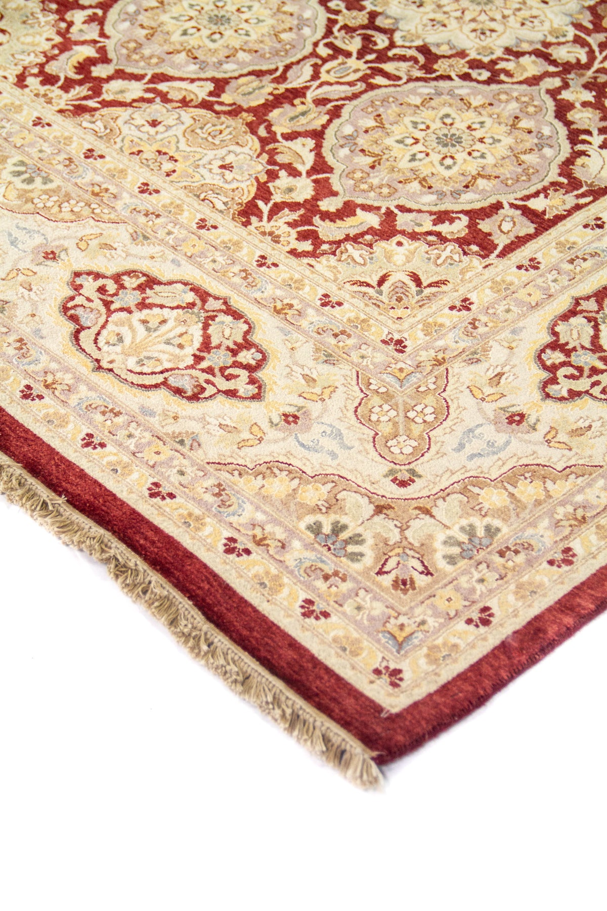 Primer plano de esquina de alfombra tradicional con diseño floral en tonos beige, rojo vino y detalles azul suave.