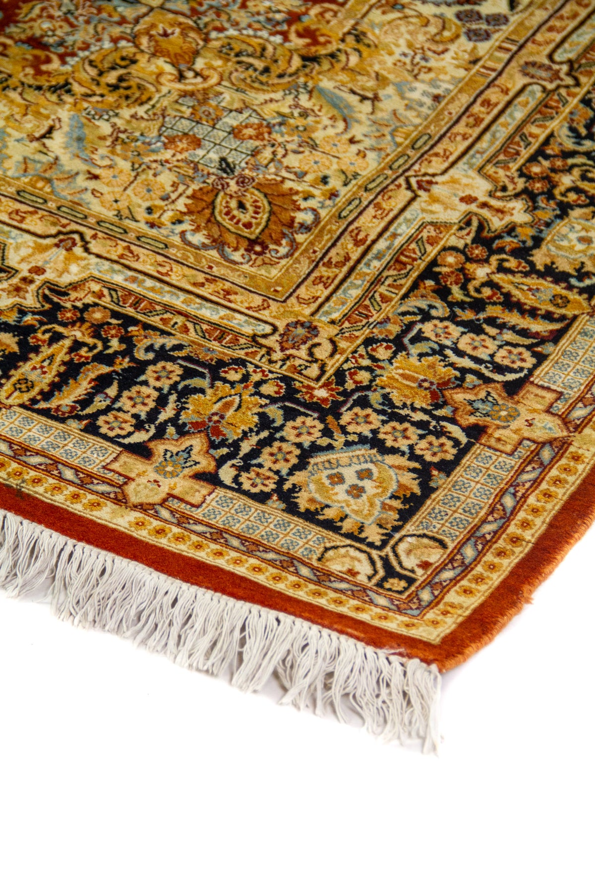 Detalle del borde de alfombra persa con patrones florales ornamentales en tonos beige, azul y negro con flecos visibles.