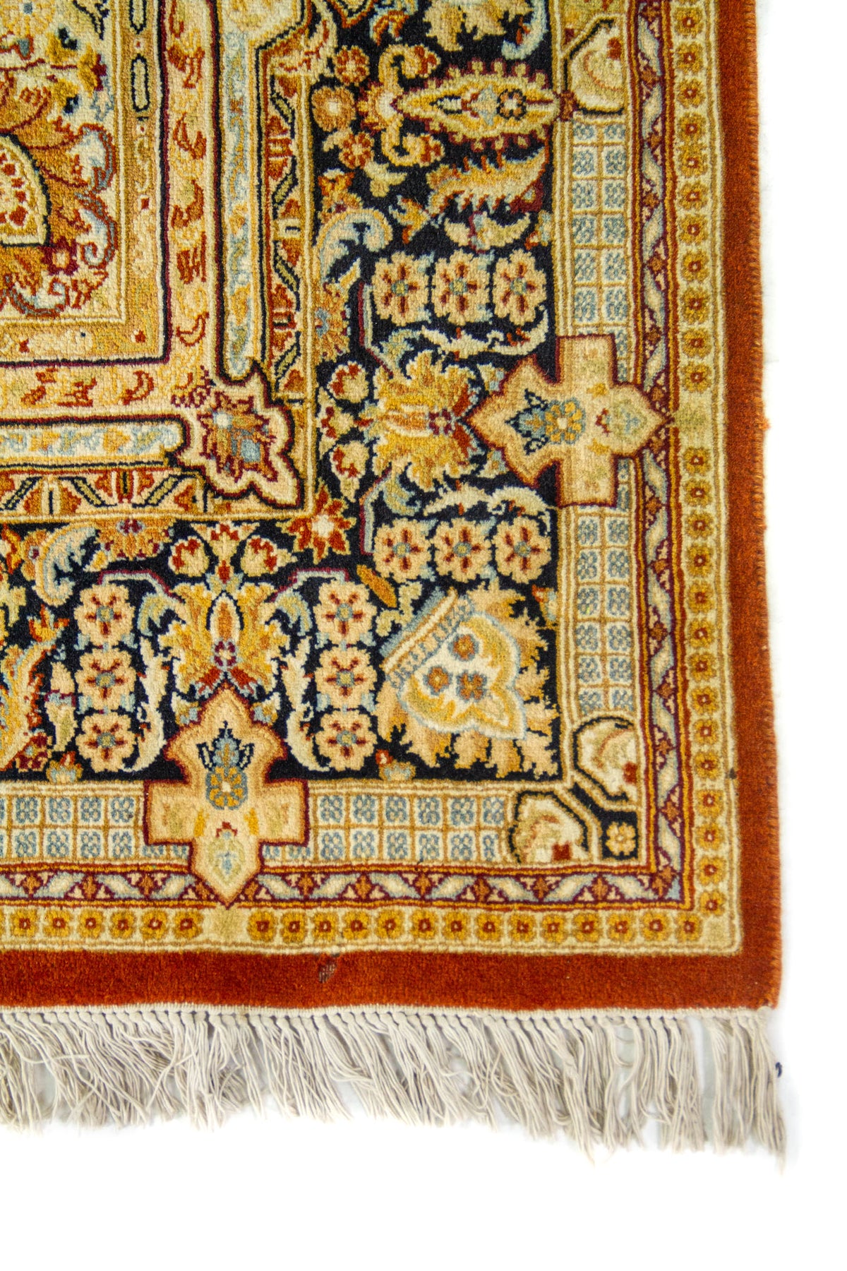 Detalle de la esquina de una alfombra persa con bordes ornamentales y flecos blancos.