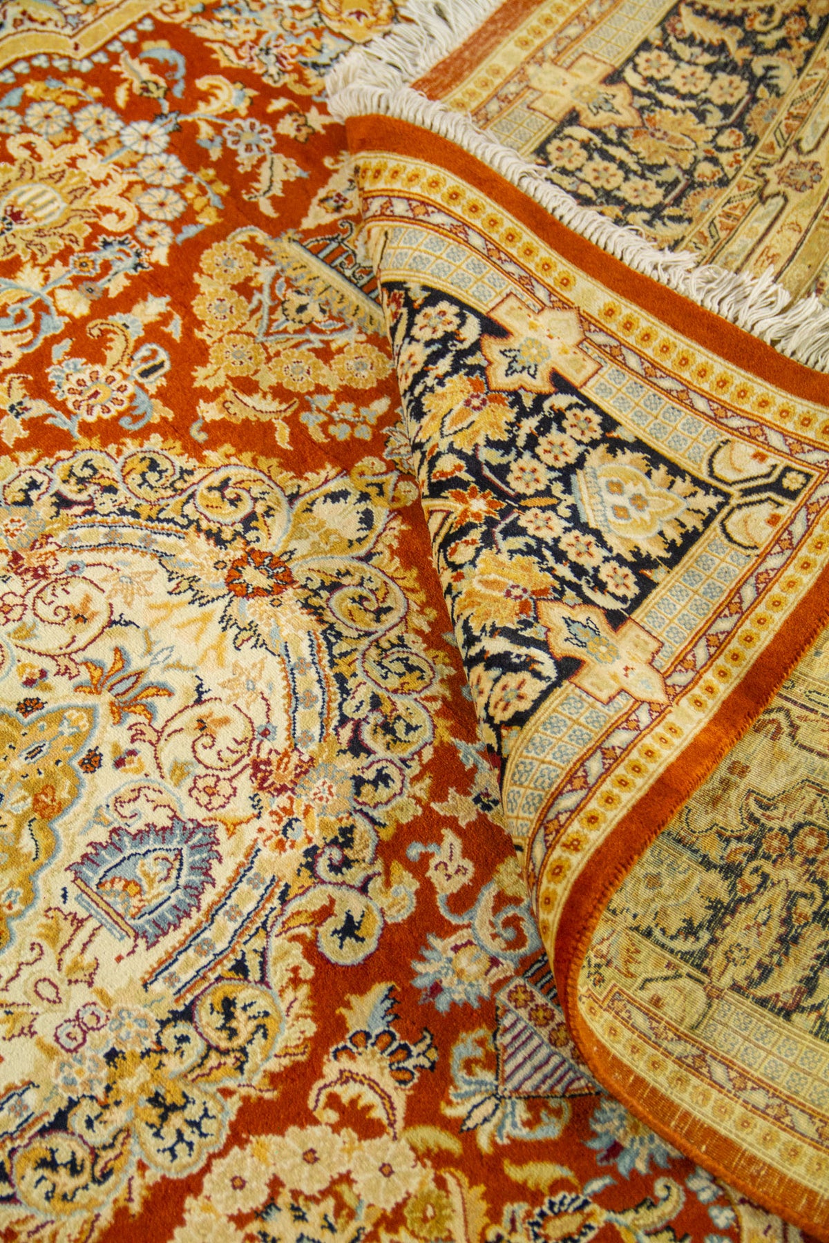 Detalle de alfombra doblada mostrando la textura del tejido y los motivos florales clásicos en rojo, azul y beige.