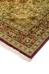 Detalle de esquina de alfombra persa con borde rojo y patrones florales ornamentales en tonos beige, azul y dorado.