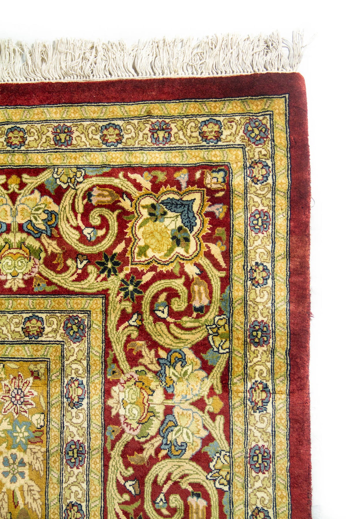 Primer plano del borde de alfombra persa con flecos blancos y diseño floral tradicional en tonos cálidos.