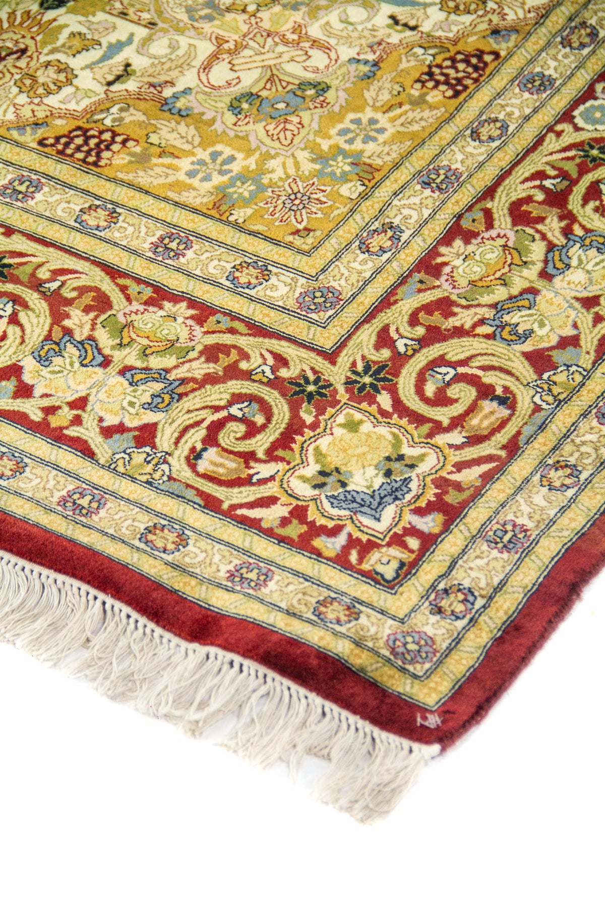 Detalle del borde y esquina de una alfombra oriental con patrones florales y guarda decorativa roja.