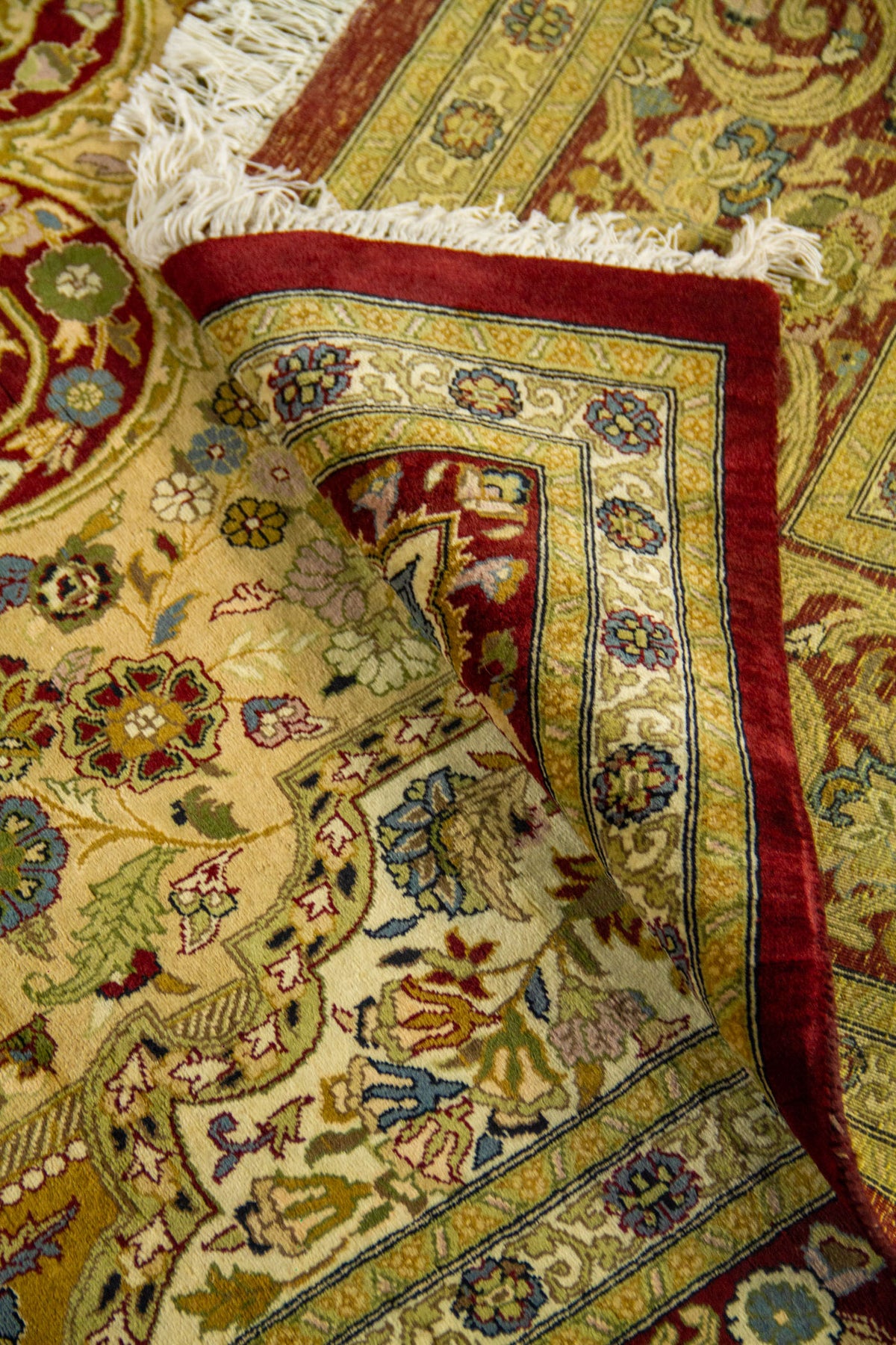 Detalle de alfombra doblada mostrando la textura del tejido y los intrincados motivos florales tradicionales.