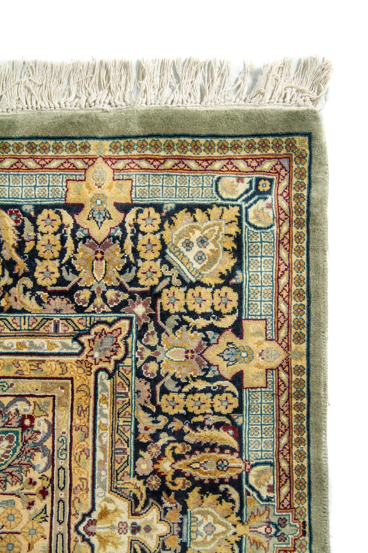 Detalle de borde superior de alfombra con guarda floral oscura, marco decorativo y flecos beige