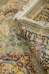 Detalle de alfombra doblada mostrando el reverso, los flecos y los motivos florales en tonos celeste, beige y azul oscuro