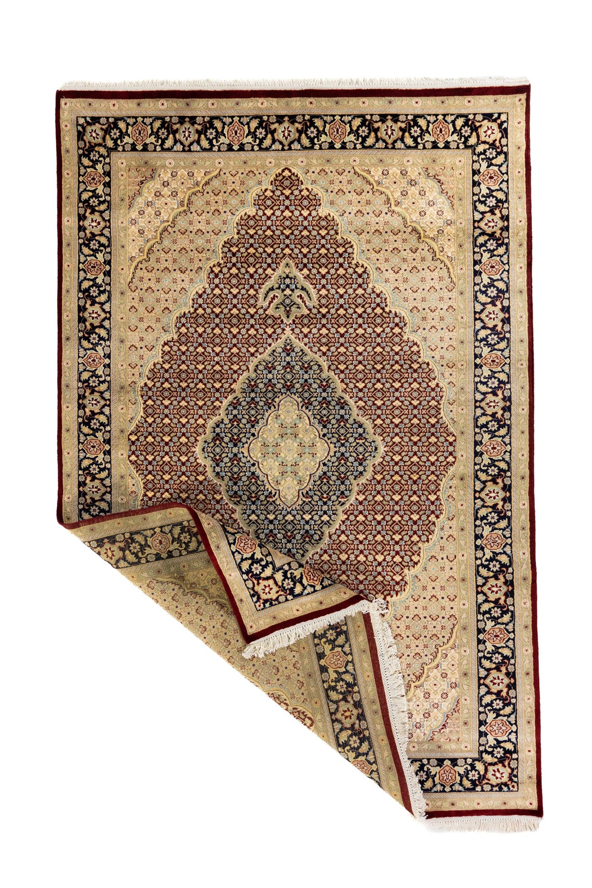 Alfombra oriental tradicional con una esquina doblada que permite ver el reverso, el grosor del tejido y los flecos en tono blanco suave.