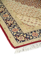 Primer plano de alfombra oriental con diseño ornamental fino, guarda floral azul marino y campo central en tonos beige, celeste y rojo oscuro.