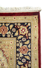 Detalle del borde superior de una alfombra con motivos florales tradicionales, flecos claros y combinación elegante de beige y azul oscuro.