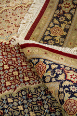 Detalle de alfombra doblada mostrando la textura del tejido, el reverso, los flecos y el contraste entre el campo central beige y la guarda oscura decorativa.