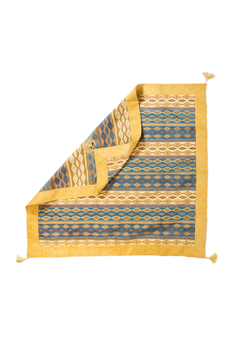 Textil decorativo beige con reverso visible, flecos y diseño geométrico en franjas