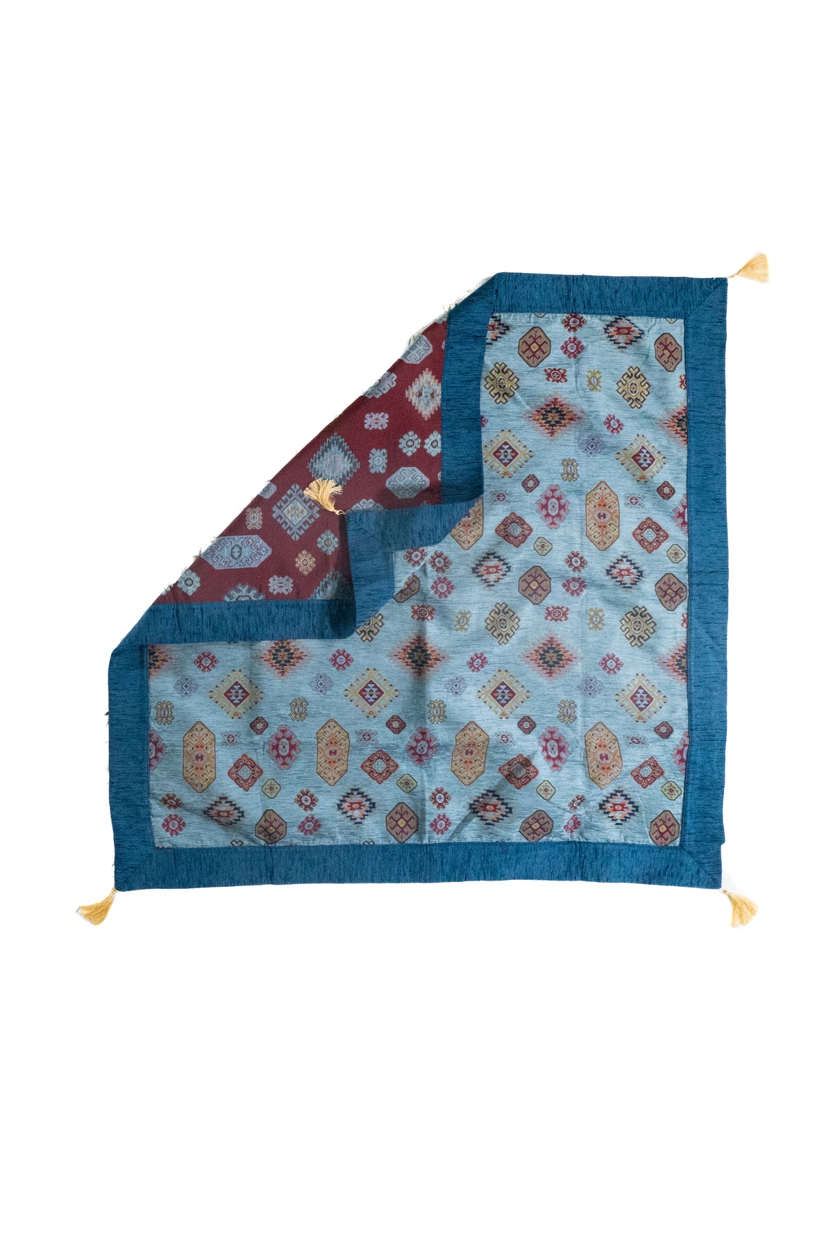 Textil decorativo celeste con reverso visible, guarda azul y flecos en las esquinas
