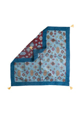 Textil decorativo celeste con reverso visible, guarda azul y flecos en las esquinas