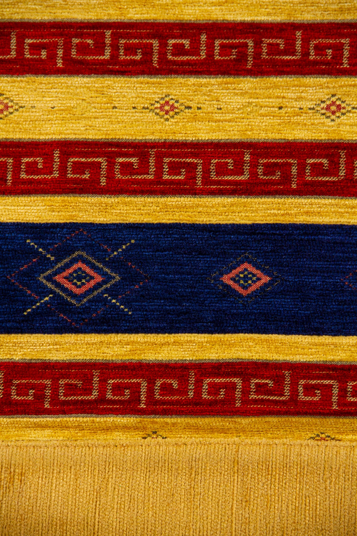 Detalle del diseño geométrico con rombos, guardas rojas y rayas azules sobre textil amarillo