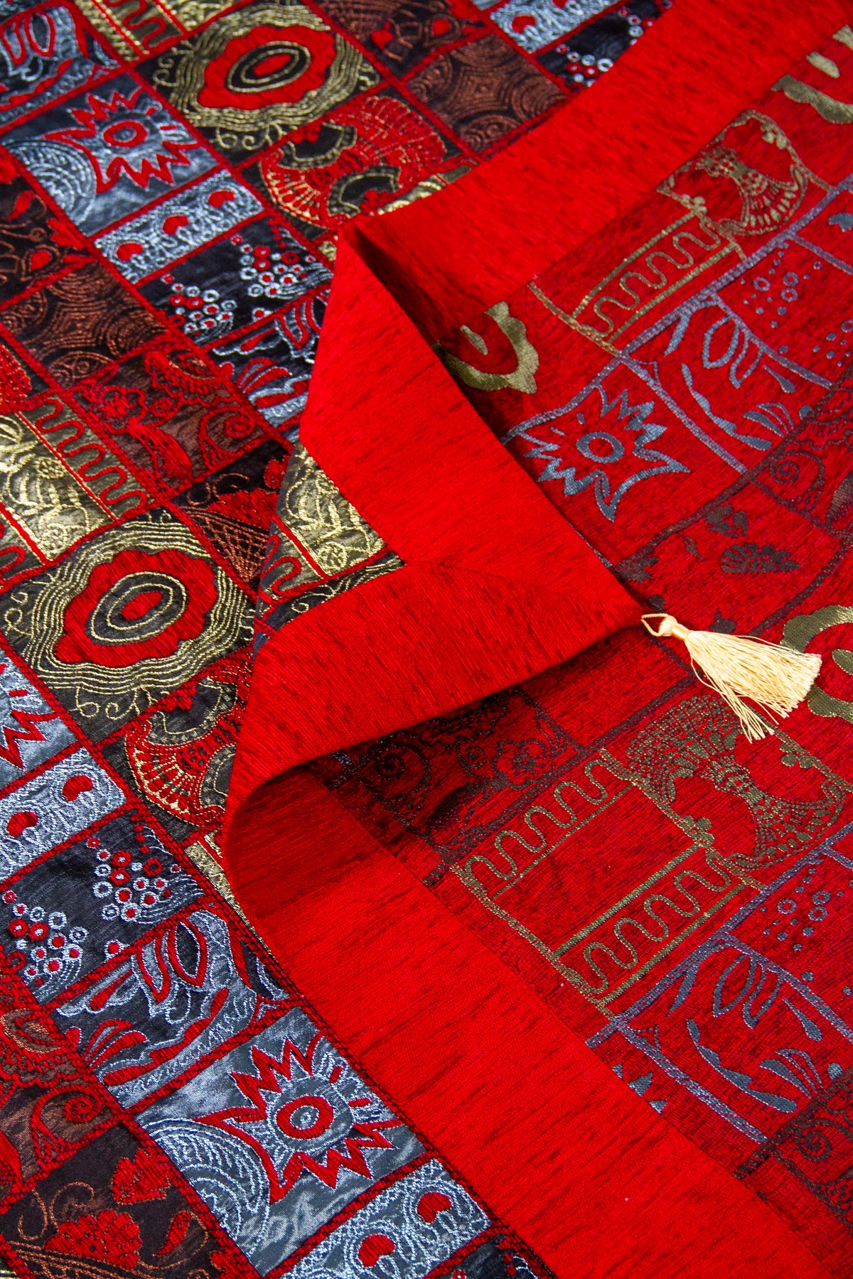 Detalle del reverso y guarda del textil decorativo rojo con diseño geométrico y fleco.