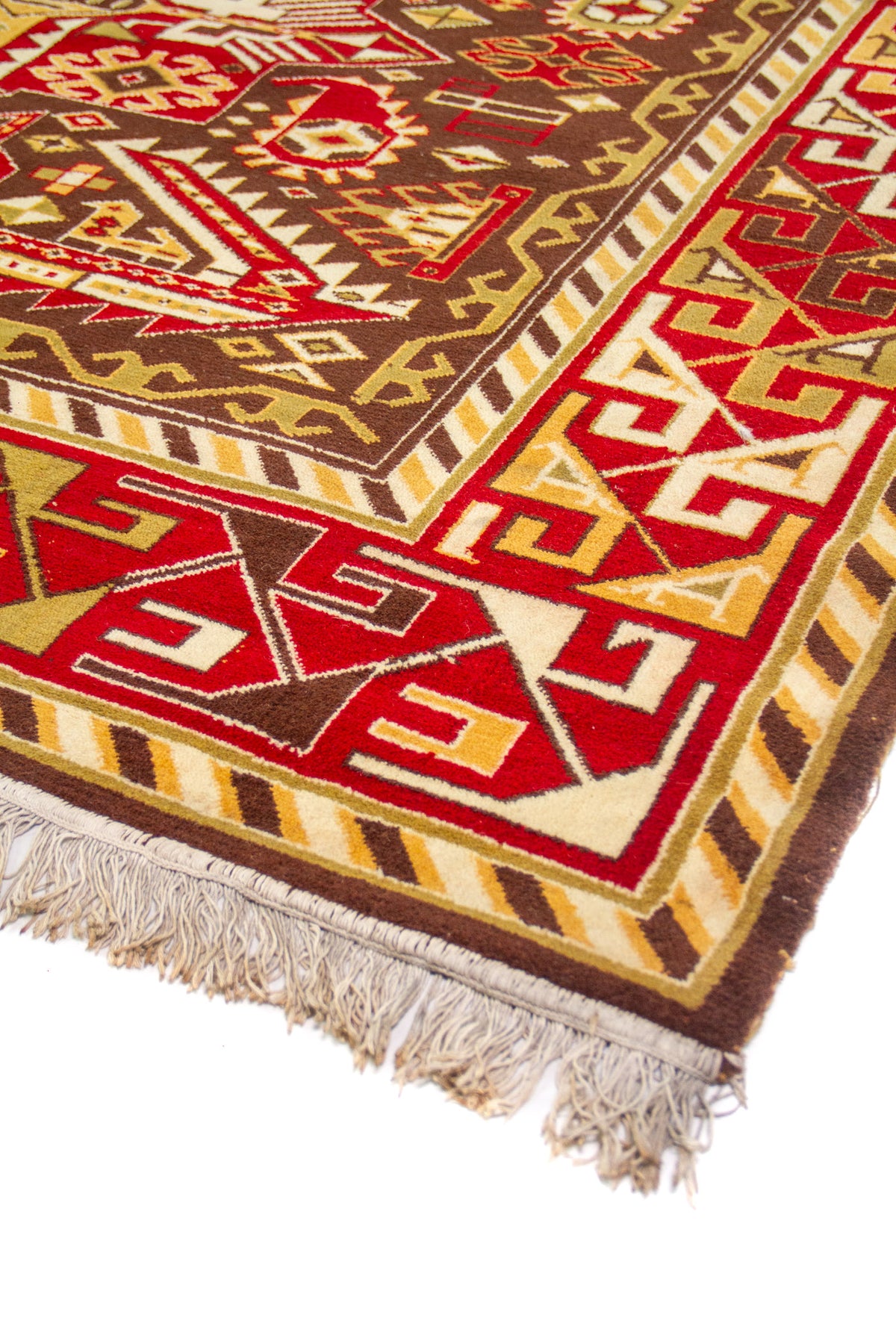 Detalle en ángulo del borde rojo y franjas en beige/amarillo, con flecos visibles en el extremo de la alfombra.