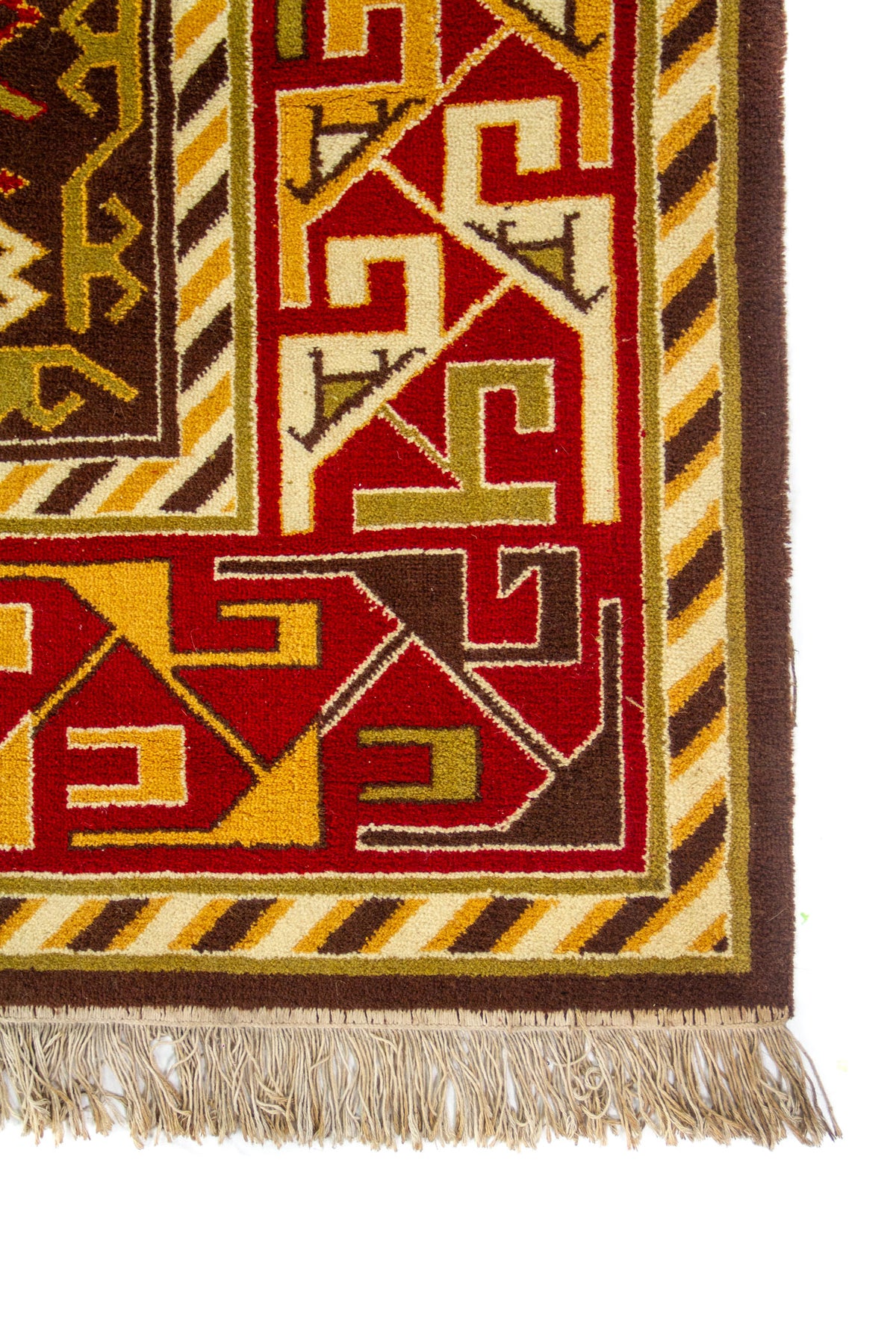 Primer plano de esquina con flecos y guardas geométricas en rojo, beige y marrón; se aprecia el grosor y el remate del borde.