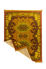 Alfombra geométrica en colores cálidos con una esquina doblada que muestra el reverso y los flecos