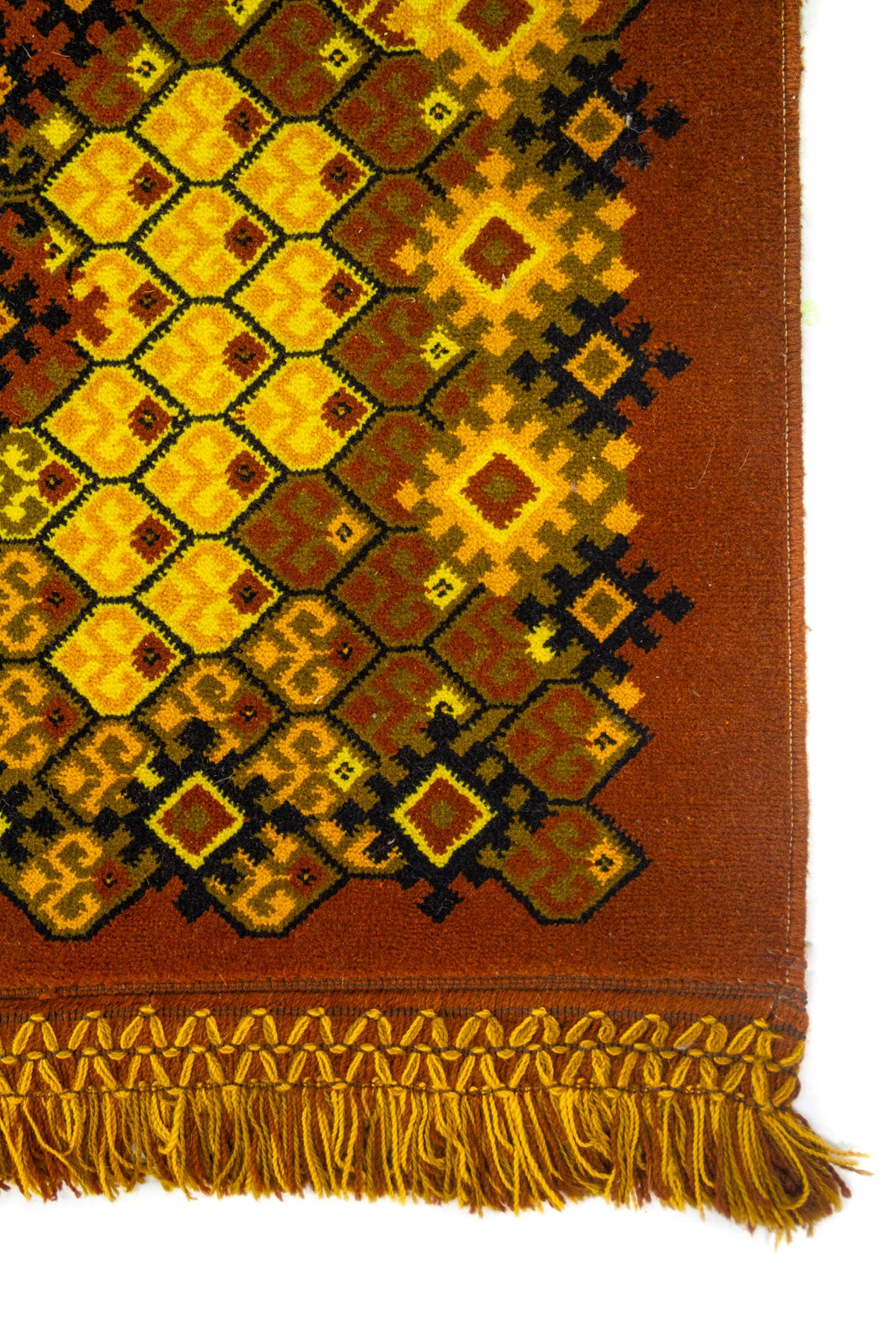 Detalle del borde de alfombra geométrica con flecos amarillo y marrón, composición de rombos y figuras escalonadas