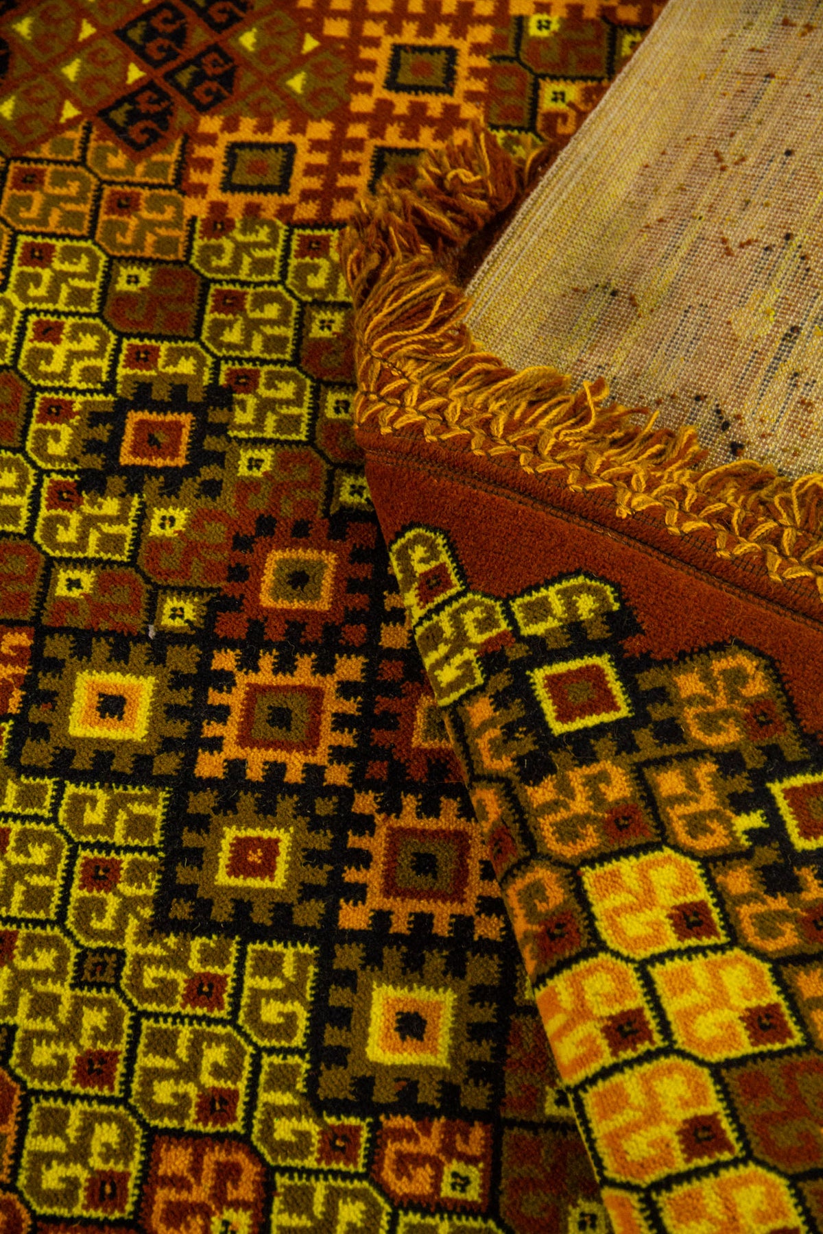 Detalle de alfombra doblada mostrando el reverso, los flecos y el patrón geométrico en tonos cálidos