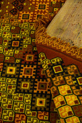 Detalle de alfombra doblada mostrando el reverso, los flecos y el patrón geométrico en tonos cálidos