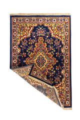Alfombra oriental azul marino con esquina levantada que muestra su flexibilidad, reverso tejido y terminación con flecos claros.