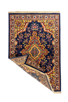 Alfombra oriental azul marino con esquina levantada que muestra su flexibilidad, reverso tejido y terminación con flecos claros.