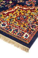 Detalle de esquina de alfombra clásica con fondo azul oscuro, bordes dorados, motivos ornamentales y flecos color beige.