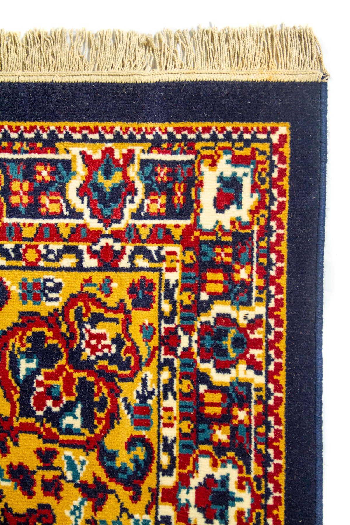 Detalle superior de alfombra clásica azul con flecos claros, guarda decorativa y patrones tradicionales de inspiración oriental.