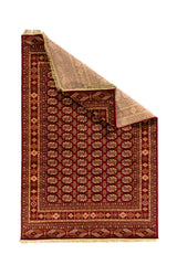 Alfombra oriental roja con esquina levantada que muestra su flexibilidad, reverso tejido y terminación con flecos claros.