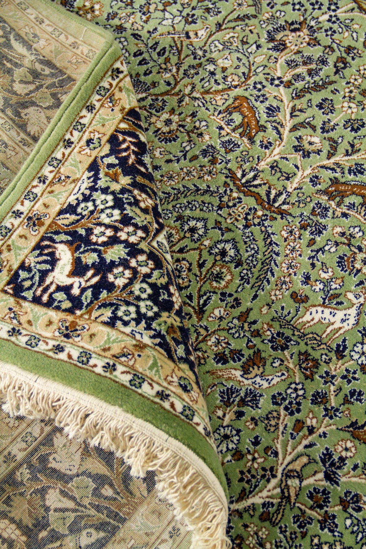 Alfombra verde doblada en detalle con patrón floral, figuras animales y textura visible