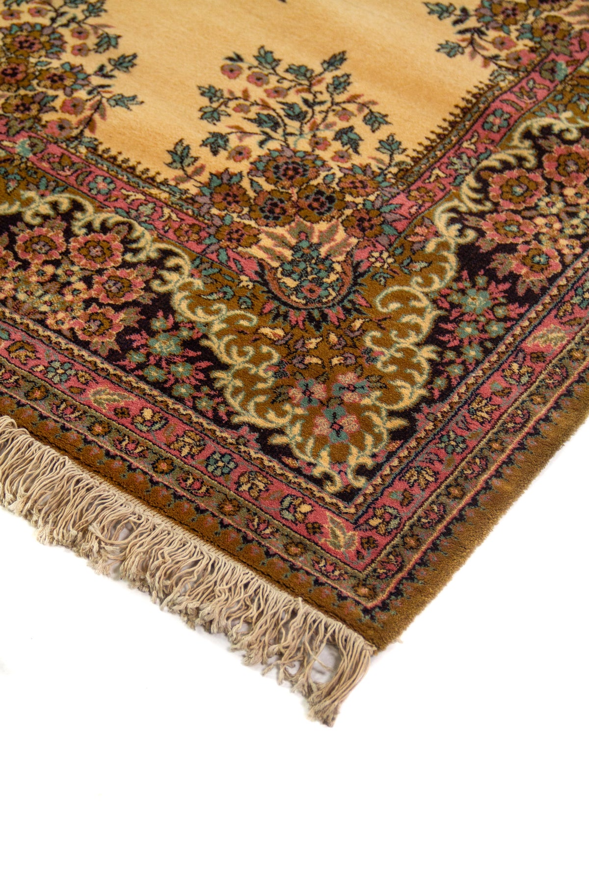 Detalle en perspectiva de alfombra clásica con fondo beige cálido, borde floral oscuro y terminación con flecos claros.