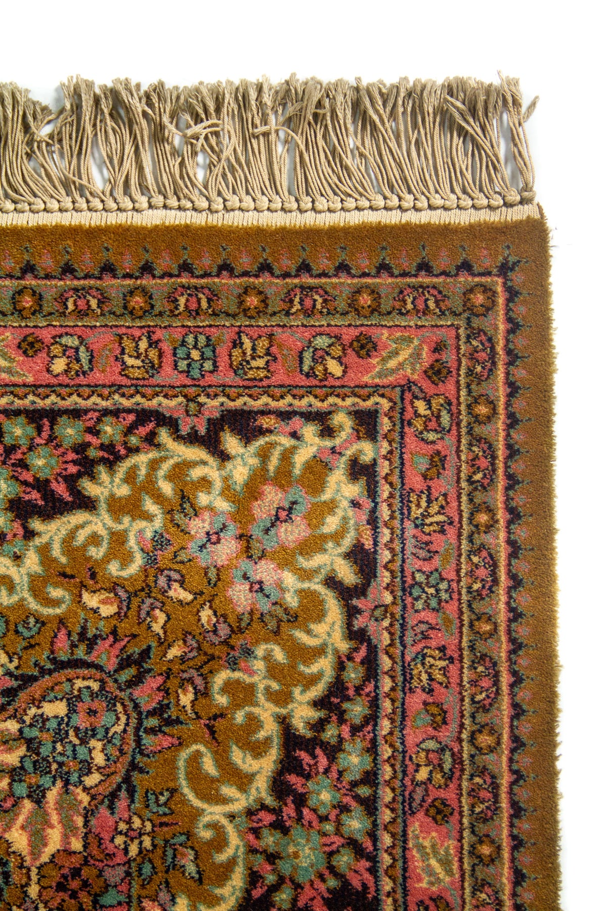 Primer plano de esquina de alfombra con flecos, borde rosa ornamental y detalles florales sobre fondo oscuro.