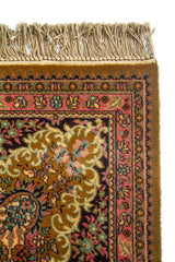 Primer plano de esquina de alfombra con flecos, borde rosa ornamental y detalles florales sobre fondo oscuro.