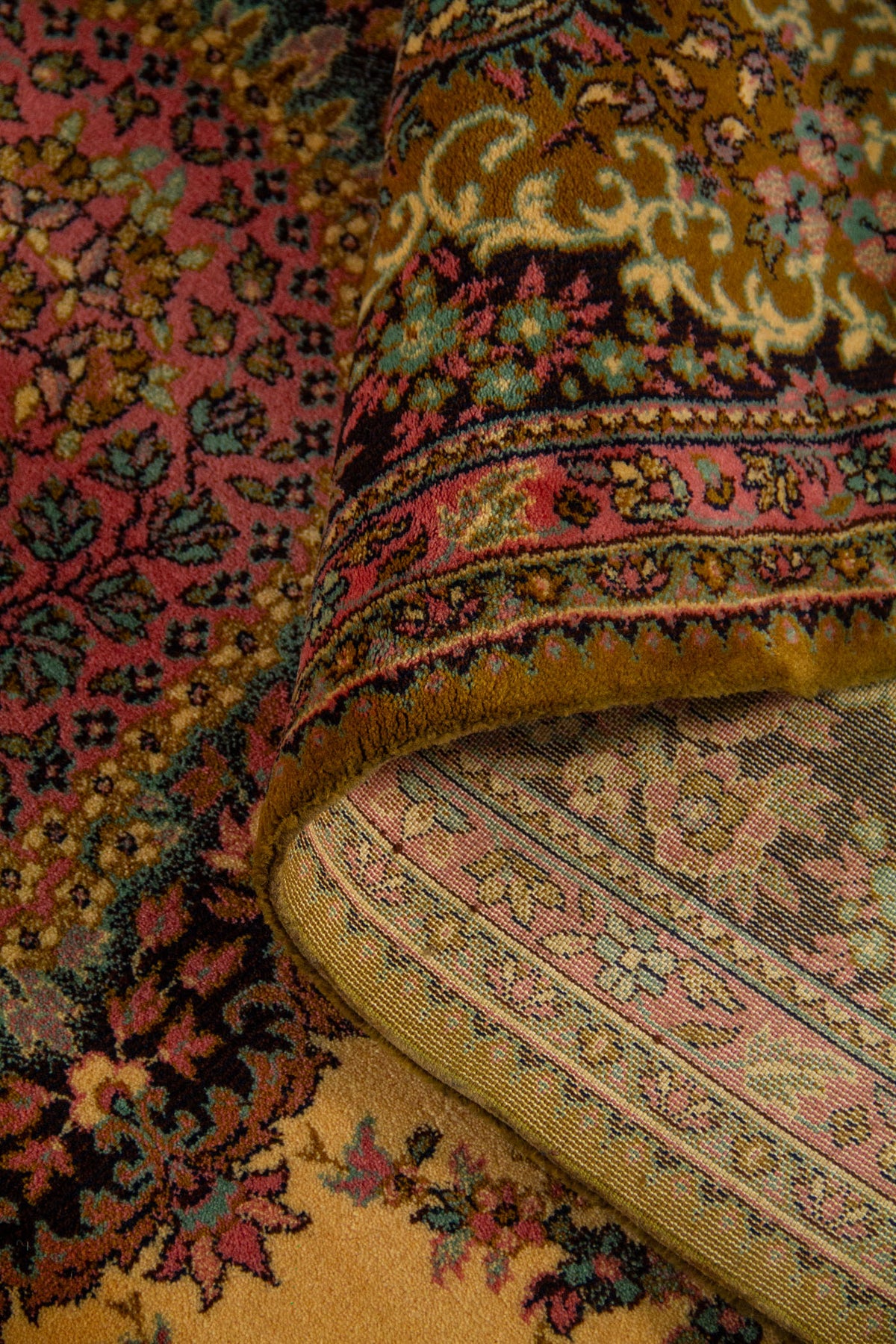 Alfombra doblada mostrando la textura del tejido, el reverso y el contraste entre el campo beige y la guarda floral oscura.