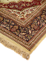 Detalle de esquina de alfombra clásica con motivos florales, fondo beige, borde oscuro ornamental y flecos color beige.