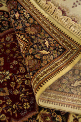 Detalle de alfombra doblada mostrando el reverso, los flecos y los motivos florales en tonos beige, rojo, marrón y dorado.