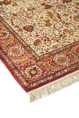 Primer plano de borde de alfombra oriental con guarda roja, ornamentos florales y delicados detalles en celeste, beige y dorado.