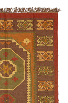 Detalle de una alfombra artesanal de lana con diseño geométrico tribal en tonos tierra y óxido.