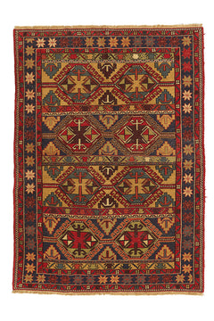 Alfombra kilim con diseño de rombos y figuras geométricas en tonos rojos, dorados y azul marino, con borde de flecos y patrones intrincados.